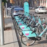 Foto d'una estació del sistema de bicicleta pública BiciPalma a la plaça Alexander Fleming amb carrer Balmes de Palma. A darrera, un cotxe elèctric endollat a un punt de càrrega. A l'esquerra, un carril bici sobre la voravia. Aquesta imatge serveix per a il·lustrar alternatives sostenibles en matèria de mobilitat i aparcament, com el bikeshare, el carsharing o cotxe compartit, una alternativa al rent a car o lloguer de cotxes convencional.